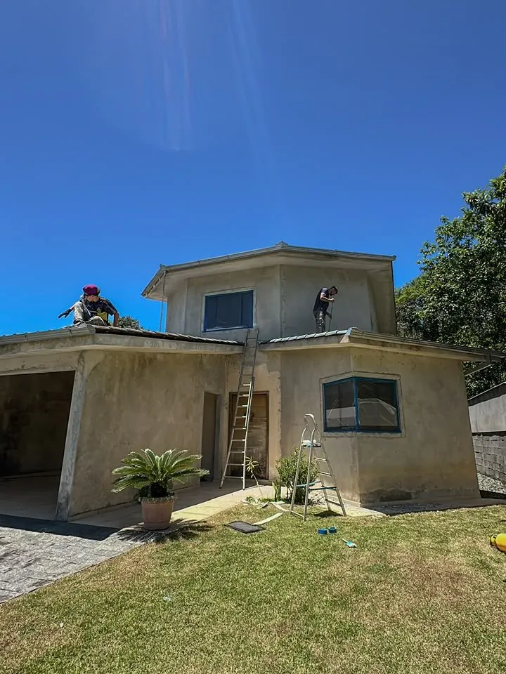 Sobrado com pintura antiga desbotada e equipe da Nova Fachada trabalhando no telhado