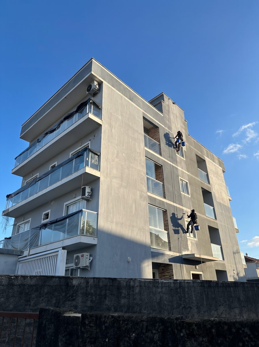 Dois pintores da Nova Fachada suspensos por corda pintando a fachada de um prédio de quatro andares
