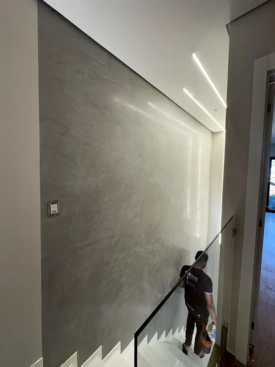 Aplicador da Nova Fachada finalizando parede de escada em cimento queimado cinza, com iluminação embutida